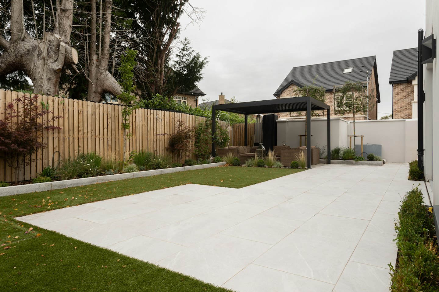 Moderner Hinterhof mit grauer Terrasse, Kunstrasen und Pergola.